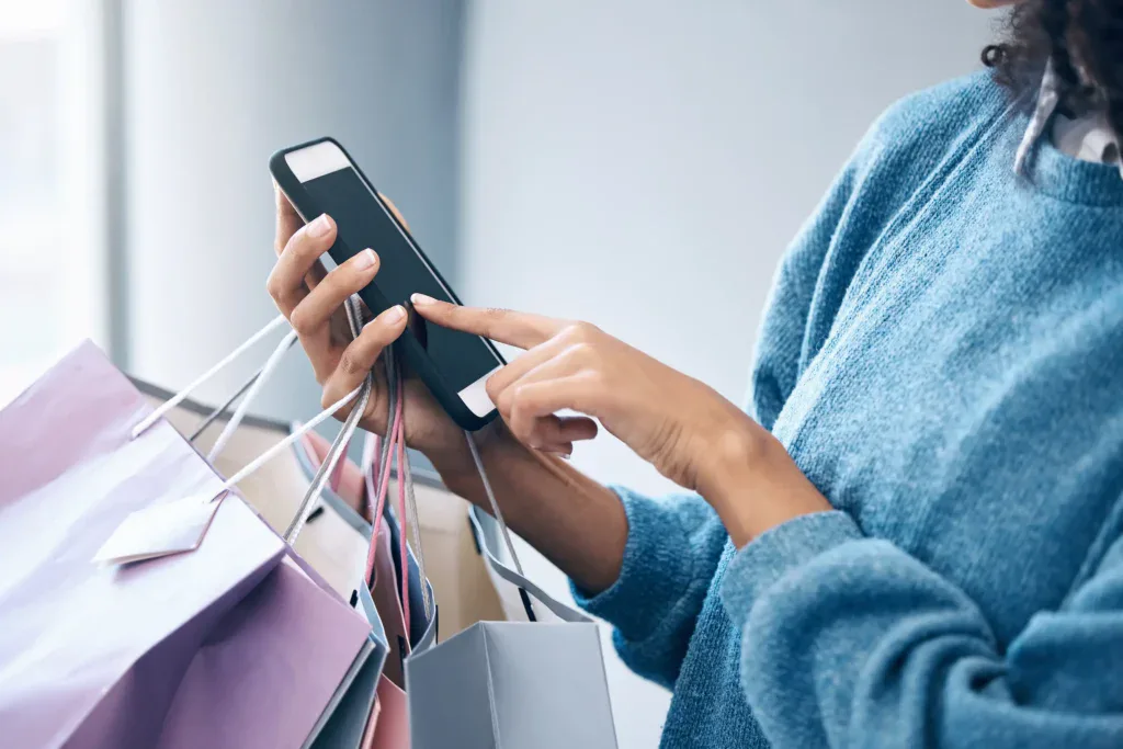 Consumidora utilizando su smartphone durante una compra, representando la integración entre comercio electrónico, experiencia de compra y retail digital. 